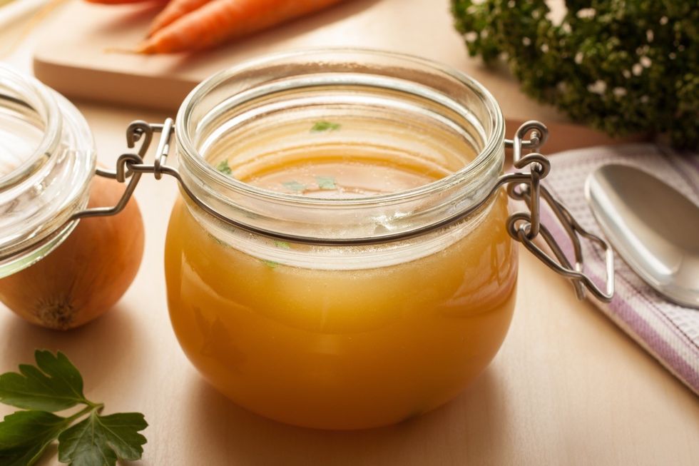 Bone made from chicken in a glass jar, with carrots, onions and parsley on the back